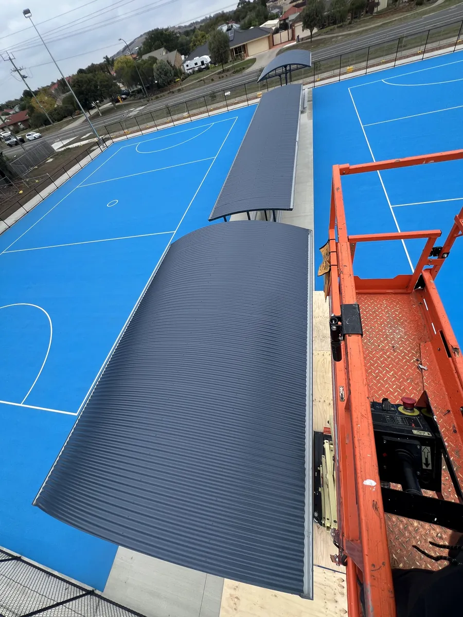 Installing a curved shelter roof from a scissor lift beside the netball courts