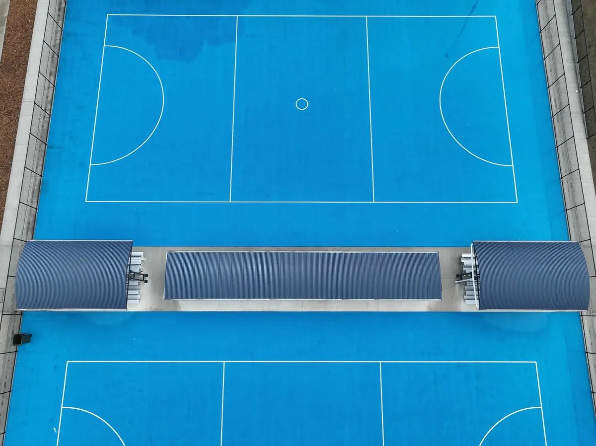 Top-down drone shot of curved shelters between blue netball courts in Sunbury